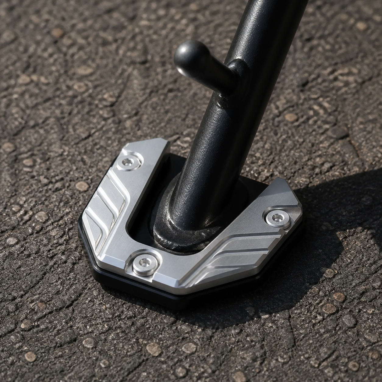 Silver CNC kickstand pad on a motorcycle side stand on asphalt