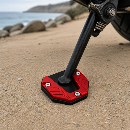 Red CNC kickstand pad supporting a motorcycle side stand on sand